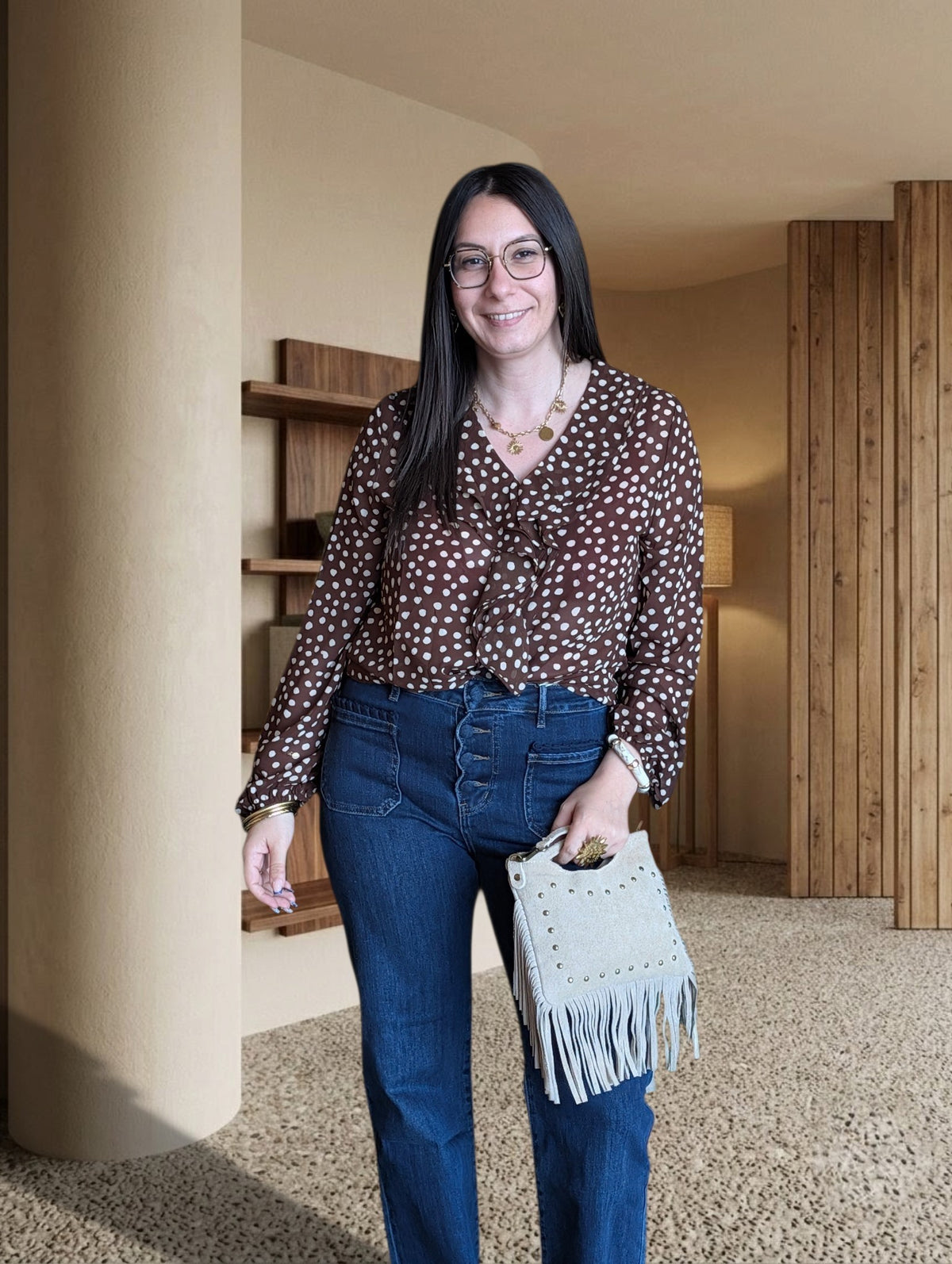 Femme portant une blouse La Roberie marron à pois en mousseline avec col à volants devant un mur végétal